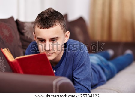 Teenage caucasian boy reading a book on the sofa, selective focus