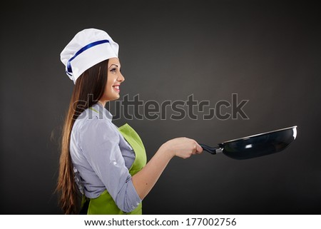 Studio shot of a young woman cook holding a wok pan over gray background