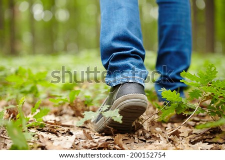 Image from the back of a man\'s feet walking through a forest on a footpath