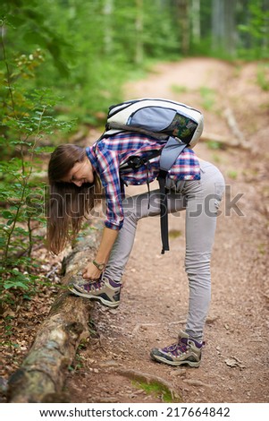 Young hiker woman with backpack on a forest trail in the mountains, lacing her boots