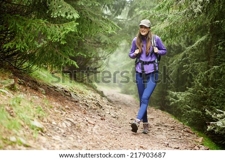 Young hiker woman with backpack on a forest trail in the mountains