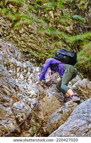 Image from the back of a young woman climbing on the rocks of a steep mountain