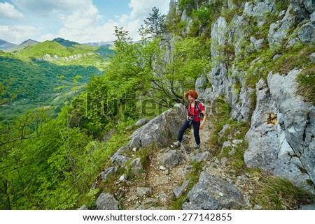 Hiker woman with backpack and camera on a trail in the mountains