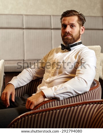 Fashionable bearded young caucasian man sitting in an armchair