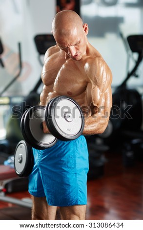 Caucasian man doing biceps curl with dumbbells in a gym with selective focus