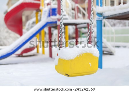 snow covered swing and slide at playground in winter