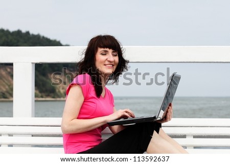Woman sitting on a bench and working by the sea with her laptop