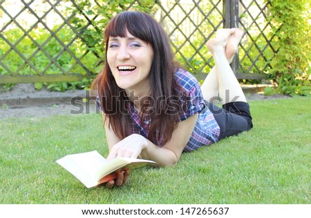 Smiling woman lying on the grass in the sunny garden and reading a book
