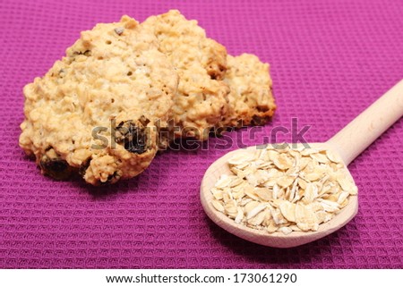 Oatmeal cookies and oatmeal on wooden spoon lying on purple background