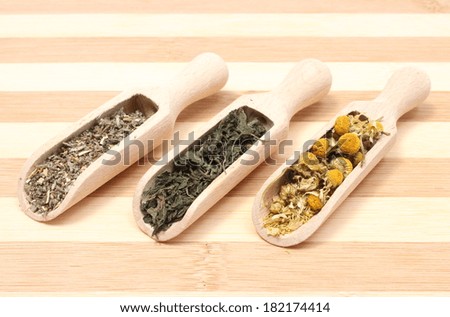 Heap of dried chamomile, nettle and sage on wooden spoons, dried herb on wooden spoons