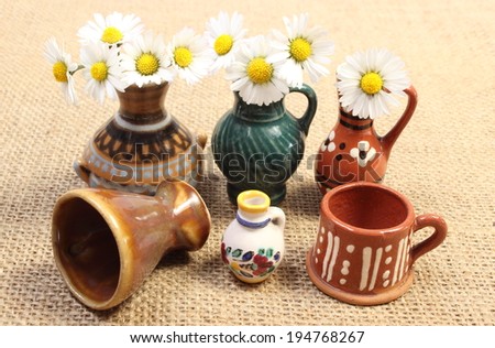 Decorative ceramic vases standing on jute canvas and fresh white daisies in glass vases