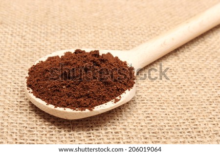 Heap of ground coffee on wooden scoop, coffee grains. Background texture of old jute