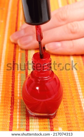 Bottle of red nail polish and hand of woman in background, nail care