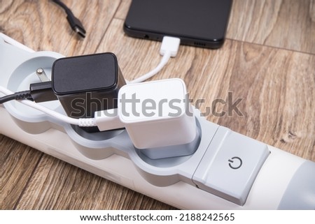 Smartphone, mobile phone and chargers connected to electrical power strip. Various devices charging concept ストックフォト © 