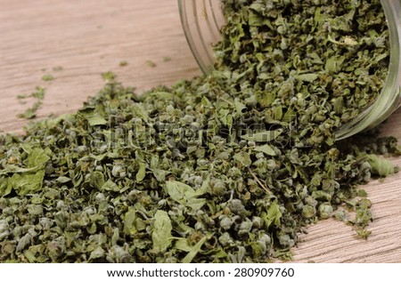 Heap of dried marjoram spilling out of glass jar on wooden background, seasoning for cooking, concept for healthy nutrition