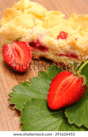 Fresh red strawberries with green leaves and piece of fresh baked yeast cake with crumble lying on wooden surface, concept of dessert
