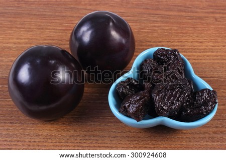 Fresh and dried plums in blue bowl lying on wooden table, concept of healthy food and nutrition
