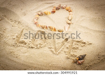 Word love written on sand at the beach and heart of shells, symbol of love, summer time