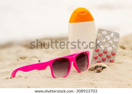 Pink sunglasses, shells, sun lotion and pills of vitamin A on sand at the beach, seasonal concept and successful tanning