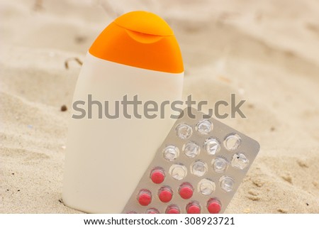 Bottle of sun lotion and pills of vitamin A on sand at the beach, seasonal concept and successful tanning