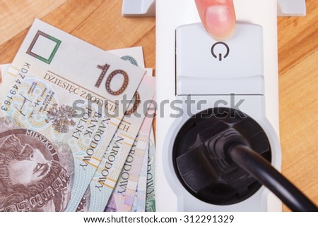 Finger of woman turns off electrical power strip with connected plug, polish currency money, concept of saving money on electricity, energy costs
