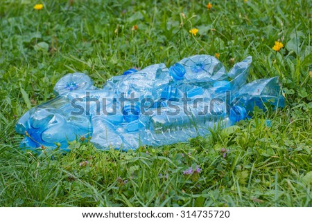 Crushed plastic bottles of mineral water and bottle caps on grass in park, concept of environmental protection, littering of environment