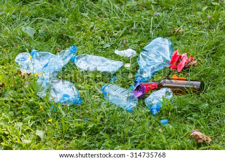 Heap of rubbish on grass in sunny park, plastic and glass bottles, bottle caps and paper, concept of environmental protection, littering of environment
