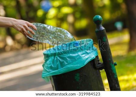 Hand of woman throwing plastic bottle into old trash can, concept of environmental protection, littering of environmental