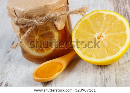 Glass jar with lemon and honey, fresh lemon and honey on wooden spoon lying on old wooden white table, concept of healthy food, nutrition and strengthening immunity
