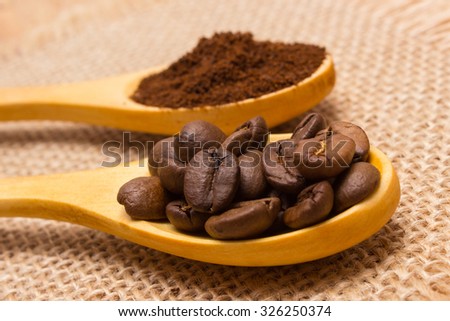 Coffee beans and ground coffee on wooden spoon lying on jute burlap, coffee grains
