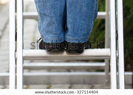 Feet of woman in black shoes on aluminum ladder in garden