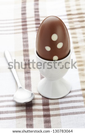 Chocolate easter egg in egg cup and spoon on brown table cloth