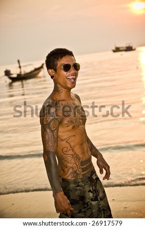 Toned man with tattoos looking out to sea during sunset