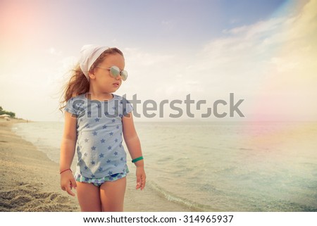 Beautiful little girl with glasses and headscarf on beach, watching the sea.\
Shallow depth of field. Selective focus.