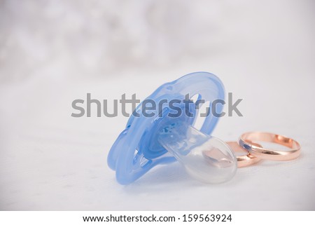 pacifier  with wedding rings on a white background with a wedding bouquet