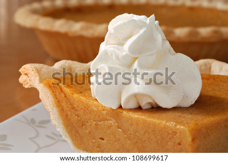 Pumpkin pie with swirls of whipped cream on decorative plate.  Whole pie in soft focus in background.  Macro with shallow dof.
