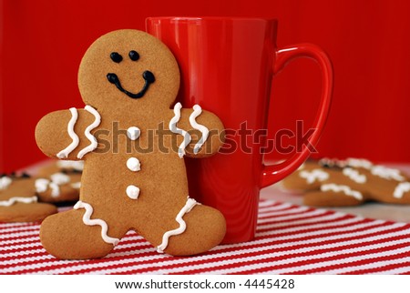 Smiling gingerbread man with red funnel mug. Additional cookies in soft focus in the background