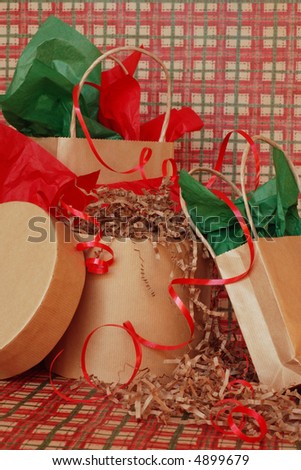 Christmas gifts in brown paper bags and boxes with green and red tissue paper and red ribbon on a sweep of plaid country style wrapping paper.