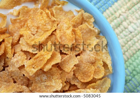 Macro still-life of corn flakes with milk in a blue bowl on color coordinated placemat.