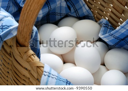 Fresh eggs in a woven basket with blue and white dish towel. Selective focus on eggs with shallow dof.  Concept - all eggs in one basket.