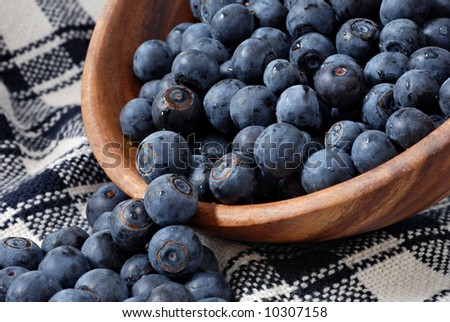 Freshly washed blueberries spilling out of a wooden bowl onto a handwoven dish towel.  Close-up with shallow dof.