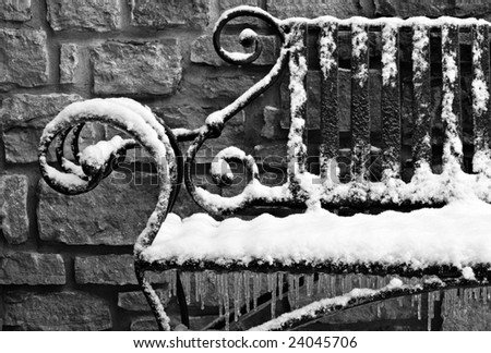 Black and white image of decorative wrought iron bench with snow and ice.