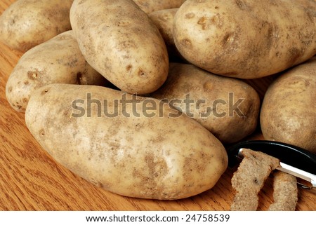 Fresh raw potatoes with potato peeler on wooden cutting board.  Macro with shallow dof.