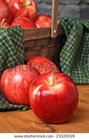 Gala apples on rustic wood with basket of apples and stone wall in background.  Close-up with shallow dof.