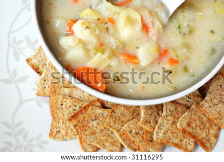 Bowl of homemade potato soup with crackers on decorative serving plate.  Macro with shallow dof.  Focus on vegetables in spoon.