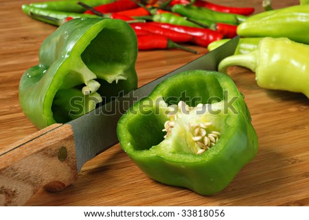 Green bell pepper with knife on bamboo cutting board.  Variety of peppers in background.  Macro with shallow dof.