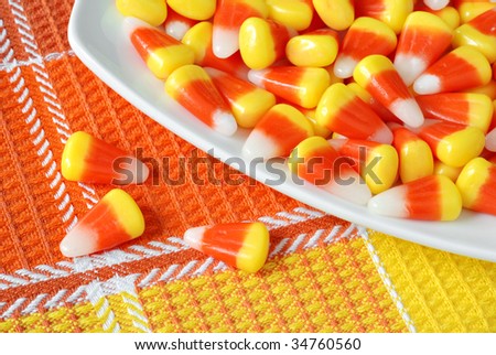 Candy corn on glass plate with color coordinated fabric background.  Macro with shallow dof.  Focus on 3 candies on fabric.