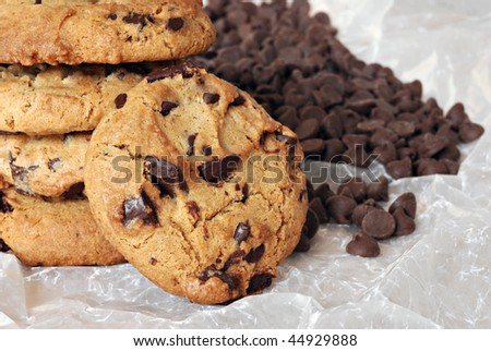Stack of freshly baked chocolate chip cookies on crumpled wax paper with extra chocolate chips in background.  Macro with shallow dof.