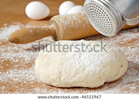 Classic wooden rolling pin with freshly prepared dough and retro flour shaker.  Shallow dof.  Selective focus on shaker and dough.