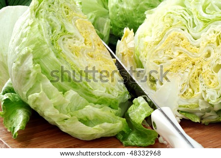 Fresh iceberg lettuce with knife and water droplets on wooden cutting board.  Macro with shallow dof.